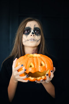 A girl with scary makeup and a halloween pumpkin