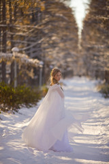 Fototapeta na wymiar beautiful girl in a white dress walks in the winter forest
