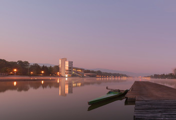 Fototapeta premium Purple dawn and a view of the Rowing canal in Plovdiv - European Capital of Culture 2019. A wooden pier and a boat near it on the mirror surface of the water. Nature in the city - concept, background.