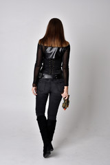 full length portrait of a pretty brunette woman wearing black leather fantasy costume with a gun....