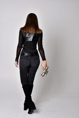 full length portrait of a pretty brunette woman wearing black leather fantasy costume with a gun....