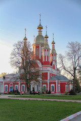 Fototapeta na wymiar Red and white orthodox church with golden domes lit by the setting sun
