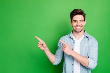 Foto op Canvas Photo of amazing salesman guy in excited mood indicating finger to empty space advising cool shopping prices wear casual denim shirt isolated green color background © deagreez