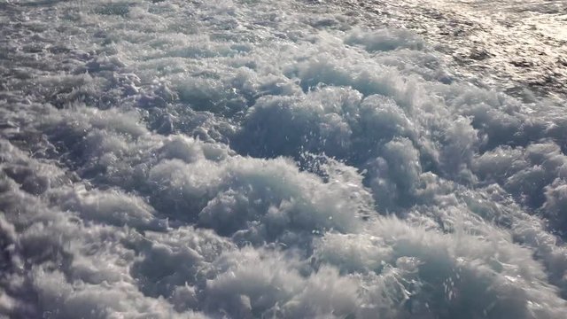 Blue ocean sea water wave with fast yacht boat wake foam of prop wash. Close up, background . Splashing drops of sea water during the movement of the ship. Concept of travel and nature