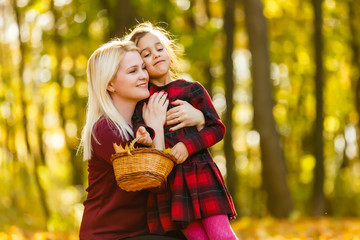 Young mother and her daughter little girl collects leaves in a autumn park