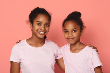 Portrait of cute little sisters embracing over pink background