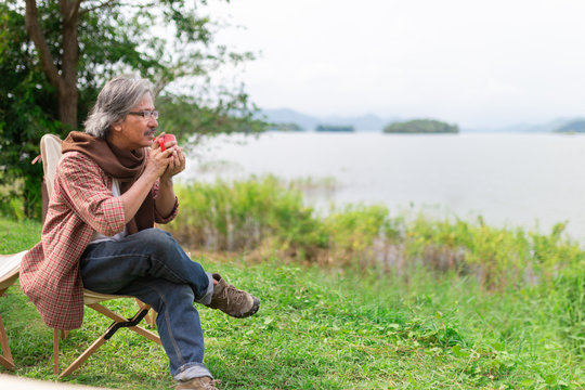 Asian Senior Man Travel In Forest, He Drinking Hot Coffee At Lakeside , Happiness Retirement Activity, Adventure And Travel