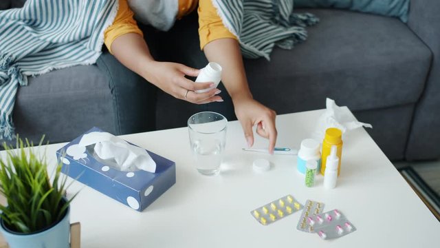 Slow motion of unhealthy young woman taking pill from bottle using medication at home sitting on couch. Modern medicine, healthcare and unhappy people concept.