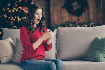 Obraz premium Photo of excited lady holding telephone reading unexpected best friends congratulation letters sitting couch in decorated garland lights room indoors wearing red sweater
