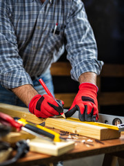 Adult carpenter craftsman wears protective gloves, with a pencil and the carpenter's square trace the cutting line on a wooden table. Construction industry, housework do it yourself. Stock photography