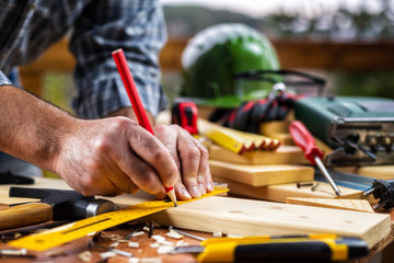 Adult carpenter craftsman with a pencil and the carpenter's square trace the cutting line on a wooden table. Construction industry, housework do it yourself. Stock photography.