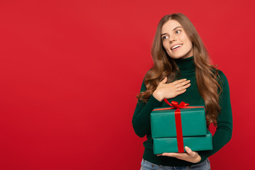 young beautiful woman in green sweater taking present and showing appreciation isolated on red background. Christmas concept