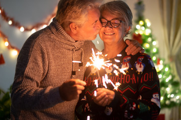 An affectionate kiss between elderly wife and husband who celebrate Christmas with sparks. Lights...