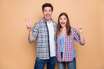 Portrait of his he her she nice attractive lovely charming funky glad cheerful cheery couple wearing checked shirt showing v-sign embracing isolated over beige pastel color background