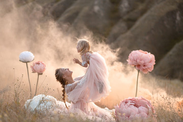 Mom and daughter in pink fairy-tale dresses play in a field surrounded by Big pink decorative flowers