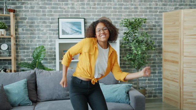 Carefree young lady African American student is having fun at home dancing listening to music looking at camera. Modern lifestyle, happiness and dance concept.