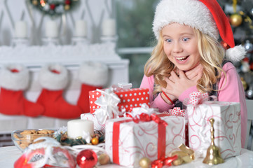 happy girl in Santa hat sitting with Christmas presents