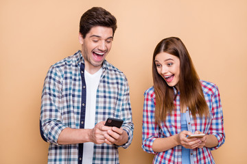 Close-up portrait of his he her she nice attractive charming ecstatic cheerful cheery glad couple wearing checked shirt using cell reading stories isolated over beige pastel color background