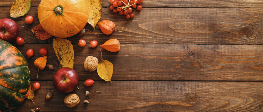 Harvest or Thanksgiving background with pumpkins, dried fall leaves, apples, red berries, walnuts on wooden table. Flat lay composition, top view, copy space