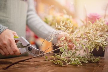 Florist girl collects bouquet of roses flowers, cuts leaves with pruning shears