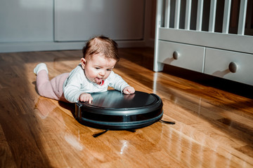 A baby with a robotic vacuum cleaner on the floor