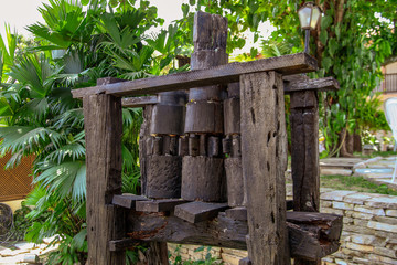 An old colonial wooden device that used to crush sugar cane to obtain sugarcane juice. In the background the landscape with palm trees