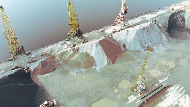 port cranes on the river bank produce sand. Port cranes with a bucket on the river bank. Extraction of river sand. Port cargo cranes extracts river sand, production. Sunset. Barge.