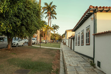 Fototapeta na wymiar Pirenopolis, Goias, Brazil, October 18, 2019: The facades of colonial-style houses with natural stone sidewalks in the late afternoon on the tree-lined streets in the historic center of Pirenopolis