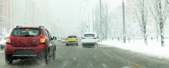 Cars drive along road with slush, snowstorm. City traffic in snow blizzard.