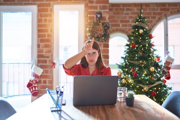 Beautiful woman sitting at the table working with laptop at home around christmas tree making fun...