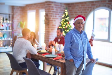 Obraz premium Senior handsome man smiling happy and confident. Standing wearing santa hat celebrating Christmas with family at home