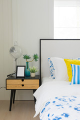 Bright bedroom interior with striped pillow on bed and bedside table lamp with picture frame on it. 