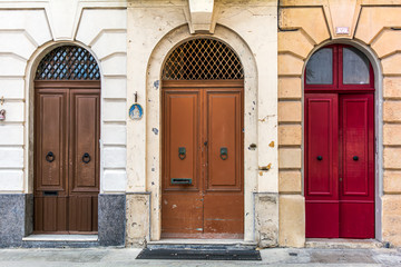 Three old wooden arched doors, brown and red, decorated with iron door knockers and molding....