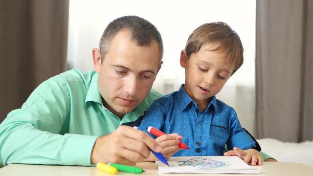 Portrait of a happy family. Father and son draw with colored markers, sitting at the table.