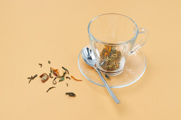 Glass tea cup with spoon and spilled herbal tea on an orange background.