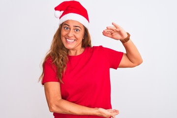Middle age mature woman wearing christmas hat over isolated background gesturing with hands showing big and large size sign, measure symbol. Smiling looking at the camera. Measuring concept.