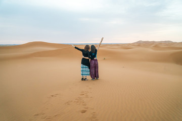 Two traveler friends holding each other and watching the sahara Desert in Morocco - obrazy, fototapety, plakaty