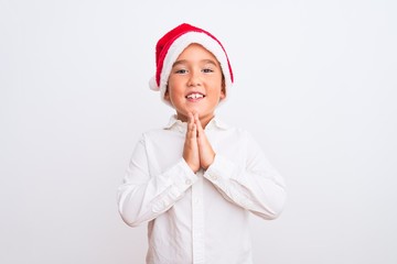 Beautiful kid boy wearing Christmas Santa hat standing over isolated white background praying with hands together asking for forgiveness smiling confident.