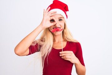 Woman wearing Christmas Santa hat holding fanny mustache over isolated white background with happy...