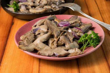 Fried mushrooms on a lilac plate stands on a beautiful wooden background