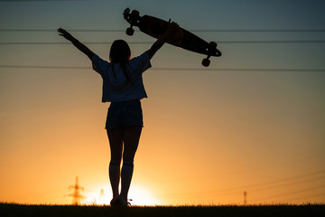 girl looks at sunset holding a longboard in her hand