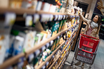 Gorgeous young woman with a shopping cart looking at some products on a supermarket aisle. Woman in the supermarket.