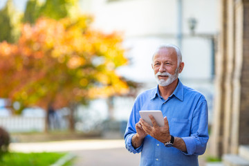 Senior man using a digital tablet outdoors. Business, technology and people concept - Senior businessman with tablet pc computer. Friendly handsome old man with tablet computer