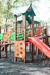 Wooden children's outdoor playground equipment slide red, orange and green color on natural background view.