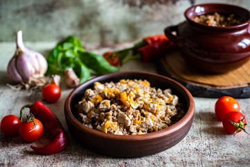 Delicious buckwheat porridge with meat and onions in a clay plate, a pot of clay with buckwheat on a gray table