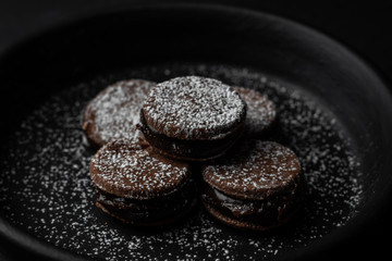 Sweet alfajores dessert cookies with chocolate over a black background