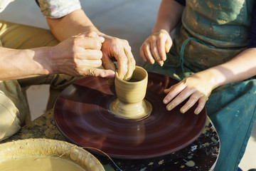 The hands of an adult man help the child to make a jug from a piece of clay on a Potters wheel.Skill