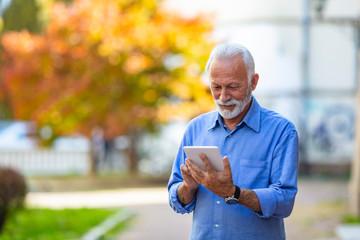 Friendly handsome old man with tablet computer. Friendly handsome old man with tablet computer. Senior man websurfing on tablet outside. Connected to a modern world