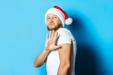 Man in a Santa Claus hat makes a repulsive gesture with his hands on a blue background. Concept no fit