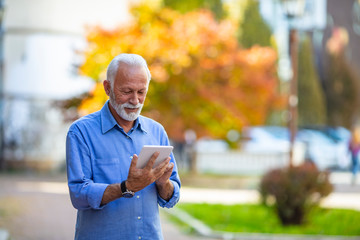 Friendly handsome old man with tablet computer. Friendly handsome old man with tablet computer. Senior man websurfing on tablet outside. Connected to a modern world